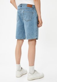 Shorts de mezclilla en azul claro, con un corte clásico, bolsillos traseros visibles y una etiqueta marrón en la cinturilla. Tejido texturizado con detalles de costura.