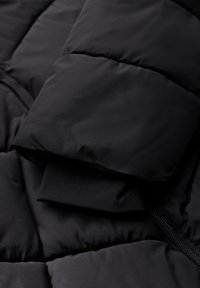 Svart puffjacka med kviltat mönster, vadderad textur, elastiska ärmslut och synlig dragkedja.