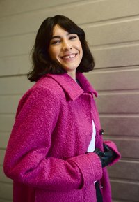 Udune, magenta värvi karvane jakk, millel on krae, eest nupud ja küljetaskud. Kandmiseks valge toppi peal, mustade kinnastega kontrasti lisamiseks.