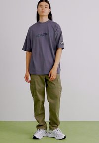 Grå oversized t-shirt med broderet design, parret med olivengrønne cargo-bukser med sidelommer og hvide sportsko.