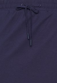 Námořnické modré plavky z hladké tkaniny s elastickým pasem, nastavitelnou šňůrkou a kovovými koncovkami na koncích šňůrky.