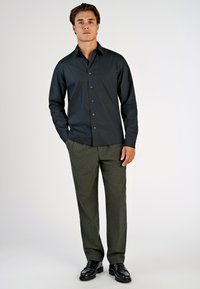 Zwarte overhemd met knopen, lange mouwen en borstzak, gecombineerd met olijfgroene broek. Zwarte nette schoenen maken de outfit compleet.