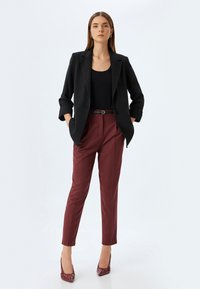 Schwarzer taillierter Blazer mit aufgerollten Ärmeln, kombiniert mit burgunderfarbenen, eng anliegenden Hosen und passenden Lackpumps, die einen eleganten Business-Look kreieren.