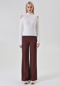 Pull en maille blanche avec un design à épaules dénudées, associé à un pantalon large marron et des baskets blanches. Le pull a une apparence texturée et duveteuse.