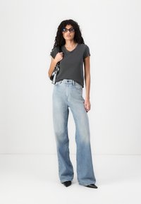 Tricou gri cu decolteu în V, combinat cu blugi largi de culoare albastru deschis cu un gradient, și pantofi negri cu vârful ascuțit. Accesoriile includ o geantă de umăr neagră.