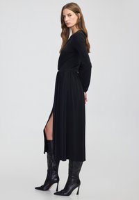 Czarna sukienka z długim rękawem, dopasowanym stanikiem, zwiewnym dołem i rozcięciem po boku. Uzupełniona przez czarne skórzane kozaki do kolan.