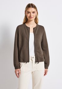 Hnědá prošívaná bunda s kulatým výstřihem, zapínáním na zip a elastickými manžetami, obsahující dvě boční kapsy a strukturovaný materiál.
