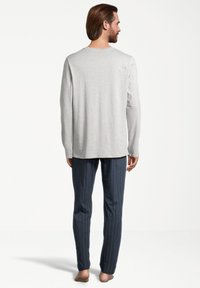 Chemise grise claire à manches longues avec un col rond, assortie à un pantalon rayé bleu marine. Le tissu semble doux ; le design est simple et discret.