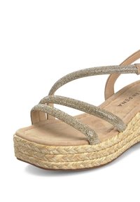 Sandale à talon compensé en ton doré avec des sangles entrecroisées ornées de strass, semelle beige texturée et plateforme en jute tressé.