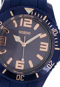 Montre en silicone bleu marine avec un cadran rond, des index en rose doré, des chiffres en relief et un affichage de la date à 3 heures.
