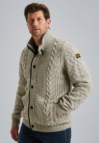 Maglione grigio chiaro lavorato a maglia con motivi a treccia, colletto alto e bottoni neri. Polsini e orlo a coste, con un patch del logo sulla manica.