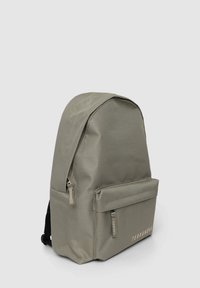 Zaino in tessuto grigio con forma arrotondata, tasca frontale con zip e nome del marchio in modo discreto nella parte inferiore. Superficie testurizzata con dettagli di cucitura.