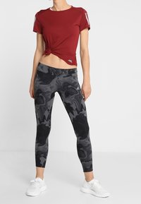 Red short-sleeve top with a knotted front, paired with black marble-patterned leggings. White athletic shoes complete the outfit.
