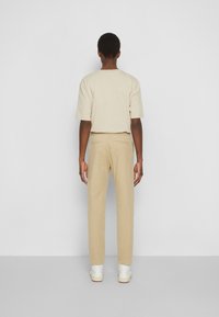 T-shirt beige à manches courtes associé à un pantalon beige et des baskets blanches. La tenue présente une coupe décontractée et un design minimaliste.