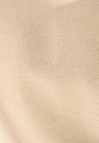 Gros plan d’un tissu tricoté beige montrant la texture détaillée des mailles et la surface douce du matériau.