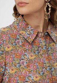 Koszula w kwiaty z kolorowym wzorem, na którym znajdują się różowe, pomarańczowe i żółte kwiaty na niebieskim tle. Zawiera klasyczny kołnierzyk i guziki.