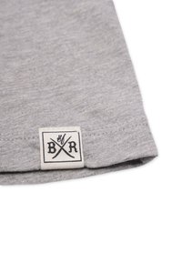 Graues Baumwoll-T-Shirt-Gewebe mit umgeschlagenem Saum. Verfügt über ein weißes gewebtes Etikett mit schwarzem grafischem Text und Symbolen in der unteren Ecke.