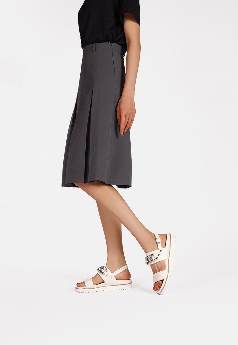 Gonna plissettata grigia chiara abbinata a sandali bianchi con una larga fascia e un accento metallico, texture liscia e suola antiscivolo.