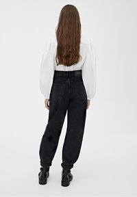 Jeans de mezclilla negros de cintura alta con piernas ajustadas, con costuras mínimas y puños enrollados, combinados con una blusa blanca de mangas abullonadas.