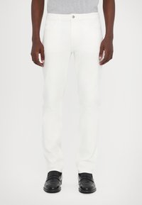 White denim pants with straight-cut design, five pockets, silver button, and stitching details, paired with black shoes.