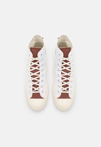 Białe skórzane sneakersy za kostkę z bordową tekstylną taśmą, białymi sznurowadłami i błyszczącymi czubkami. Gładka faktura z kontrastującymi elementami.