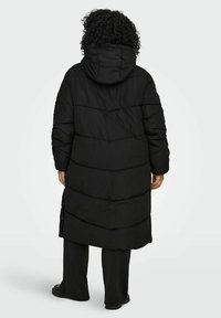 Melnas krāsas ilga, polsterēta virsjaka ar kapuci, kurai ir horizontālas šūtas joslas un sānu rāvējslēdži. Materiāls izskatās mīksts ar matētu virsmu.