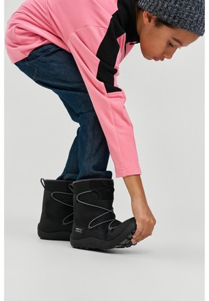 Stivali invernali neri con dettagli grigi, suola testurizzata e sistema di allacciatura. Un bambino con una maglietta rosa allaccia il proprio stivale mentre è piegato in avanti.