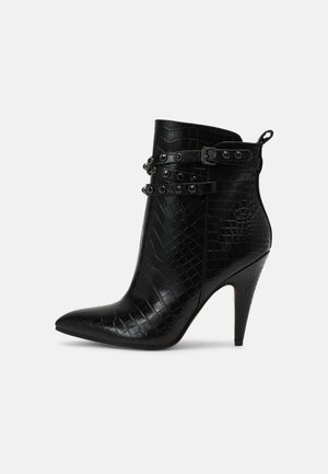 Bota de tacón alto negra hasta el tobillo, con punta puntiaguda, textura de cocodrilo y correas decorativas de doble hebilla con ojales metálicos.