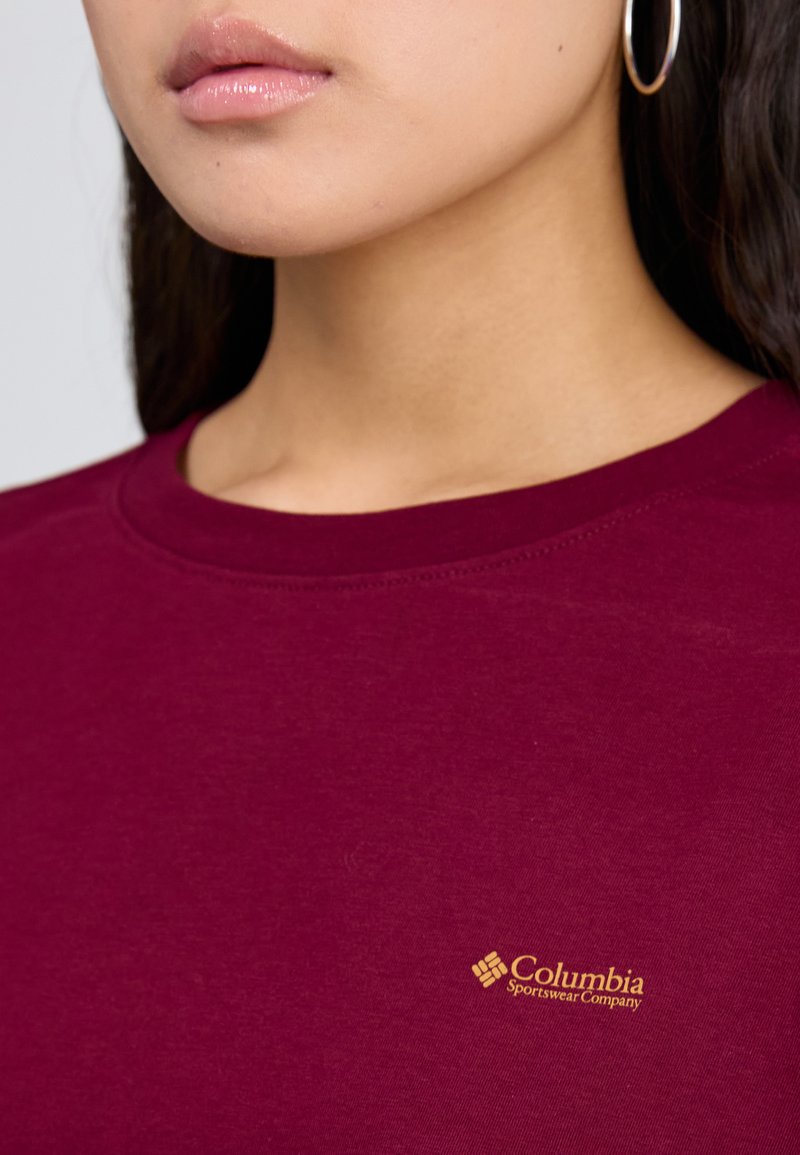 Burgundowa bluza z okrągłym dekoltem, o miękkiej fakturze, z małym złotym logo "Columbia Sportswear Company" na klatce piersiowej.