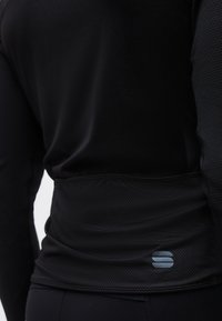 Κοντινό πλάνο ενός ατόμου που φοράει μαύρο υφασμάτινο μακρυμάνικο ρούχο με ένα μικρό γκρι λογότυπο στο κάτω πίσω μέρος.