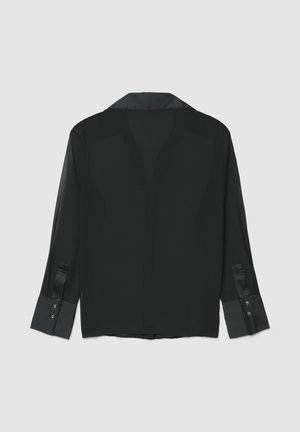 Chemise noire transparente avec col et poignets en satin, manches longues, boutons sur les poignets, et silhouette décontractée.