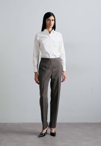 Bílá košile s límečkem, šedé kalhoty na míru, elegantní černé vysoké podpatky; hladká tkanina, padnoucí design a rovný střih siluety.
