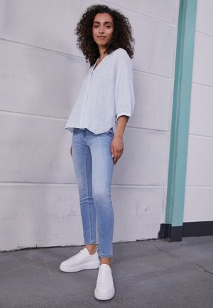 Camisa azul clara com riscas, de botões e mangas três quartos, combinada com jeans skinny azul claro e ténis brancos. Texturas suaves, estilo casual.