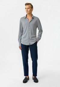 Grijze langarmige overhemd met knopen en een kraag, gecombineerd met marineblauwe slim-fit broek en donkergekleurde loafers; gladde textuur en eenvoudig ontwerp.