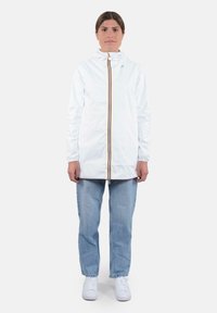 Giacca leggera bianca con zip completa e un dettaglio arancione, abbinata a jeans azzurri chiari e sneakers bianche.