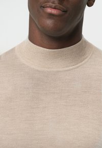 Beige ronde hals gebreide trui met een geribde kraag. De stof lijkt zacht en glad, met een eenvoudig, ongecompliceerd ontwerp.