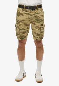 Camo cargo shorts i khaki, grøn og brun med lommer, et bælte og en afslappet pasform. Båret med hvide sokker og sneakers.