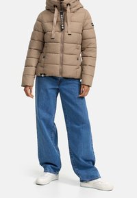 Gewatteerd jack in lichtbruin met een capuchon, voorzien van een ritssluiting aan de voorkant, trekkoorden en twee zijzakken, gecombineerd met losse blauwe jeans.