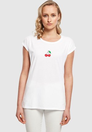 T-shirt en coton blanc avec des manches courtes roulées, présentant un petit motif de cerise rouge avec une feuille verte positionnée au centre de la poitrine.