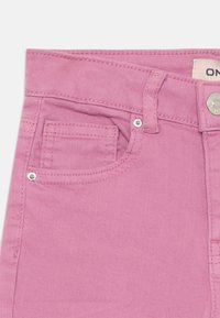 Rosa denim bukser med en lille frontlomme, sølvhardware og syninger langs bæltet og lommekanterne.