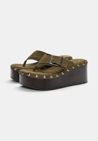 Olive green suede platform sandals with a wooden base, featuring a strap and buckle design, and metallic studs along the edge.