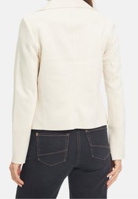 Light beige tailored jacket with a fitted design and structured shoulders, featuring long sleeves and a smooth texture.