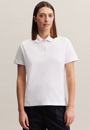 Hvid polo shirt lavet af bomuld med klassisk krave, korte ærmer og to-knap lukning. Glat tekstur, afslappet pasform.