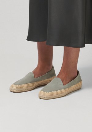 Nohy v šedých espadrilkách na nazouvání s pletenými podrážkami z provazu a černý lem sukně viditelný nad kotníky.