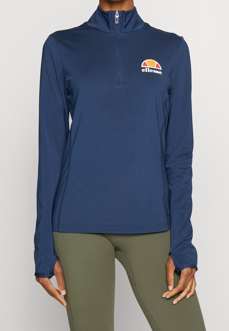 Marinblå långärmad topp med kvartslång dragkedja, mjukt tyg, med en broderad flerfärgad logotyp på bröstet och tumhål vid ärmsluten.