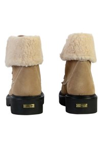 Stivali alla caviglia in suede beige con un risvolto in pelliccia sintetica crema, suola in gomma nera e dettagli in oro sul tacco.