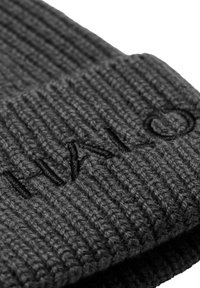 Donkergrijze gebreide beanie met ribbelstructuur. Voorzien van een opgerolde rand met geborduurde zwarte letters, wat een subtiele merkdetail toevoegt.
