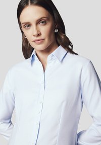 Jasnoniebieska koszula z długim rękawem wykonana z teksturowanej tkaniny, z kołnierzykiem w kształcie pointu oraz białymi guzikami z przodu.