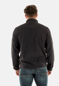 Sudadera de borreguillo negra con cuello alto, con una textura suave y un diseño sencillo, combinada con unos vaqueros de mezclilla azules.