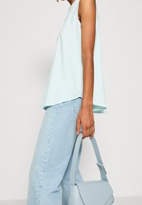 Haut sans manches bleu clair avec un design fluide, associé à un jean bleu clair à jambes larges. Tenant un sac assorti à la forme structurée.